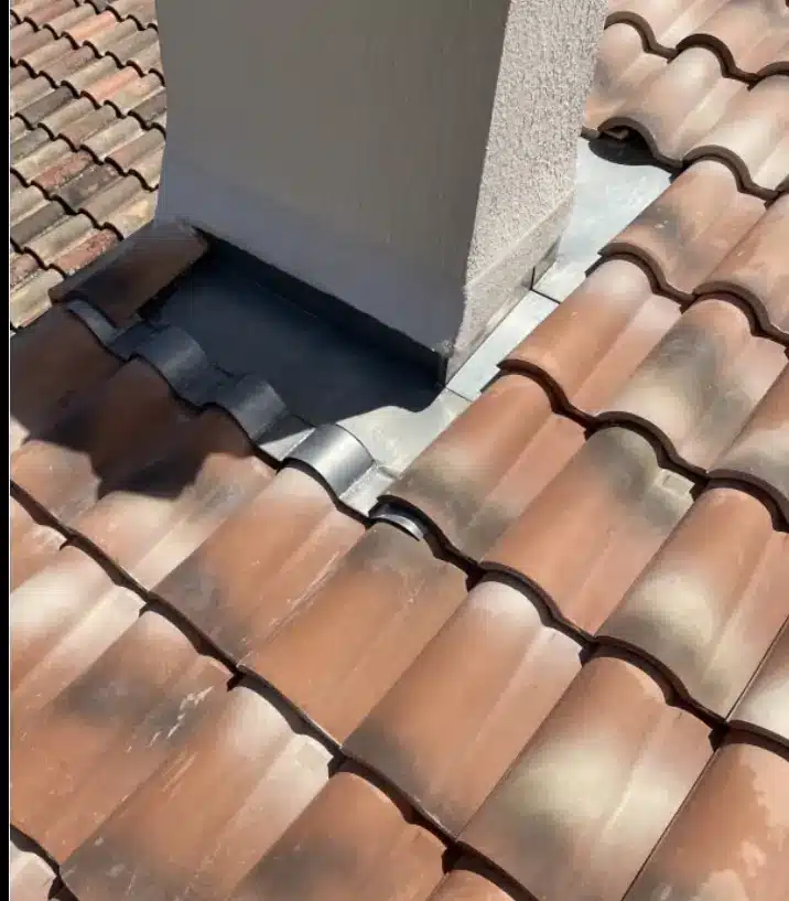 Détail du solin en plomb autour d'une cheminée en stuc beige sur un toit en tuiles de terre cuite incurvées. Étanchéité de la pénétration du toit.