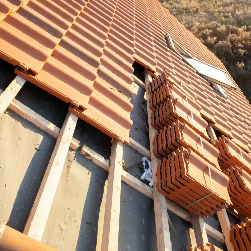 Rénovation de Toiture : Pose de Tuiles en Terre Cuite Pose de tuiles en terre cuite rouge sur charpente en bois lors de la rénovation d'une toiture avec fenêtre de toit.